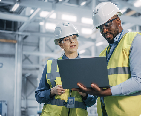 Two people in hard hats looking at a laptop in a manufacturing plant
